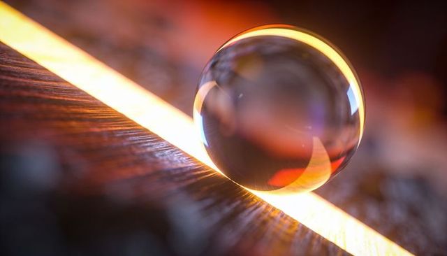 Resting glass sphere refracting warm led light on wooden surface with amber bokeh glow