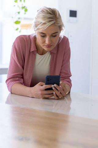 Woman leaning on glossy countertop checking smartphone in bright modern kitchen