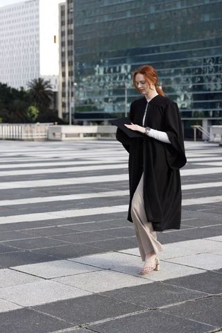 Graduate walking across modern urban plaza holding mortarboard cap