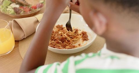 Child twirling spaghetti with meat sauce at cozy casual family dinner table