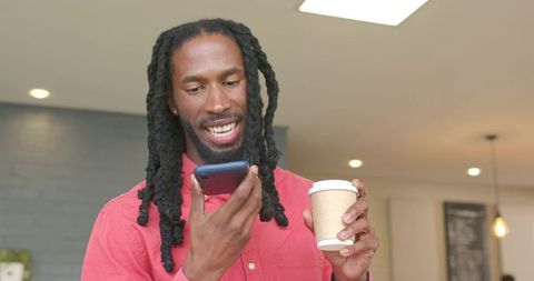 African american man speaking into smartphone holding coffee cup in casual cafe interior