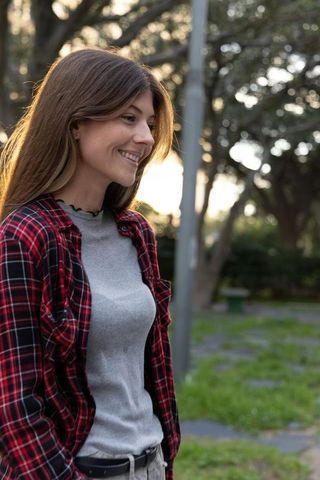 Smiling young woman enjoying golden-hour in park wearing plaid shirt and casual outfit