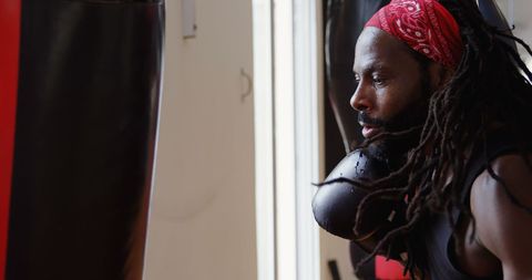 Concentrated male boxer training with punching bag in gym