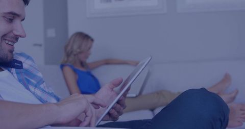 Young Couple Relaxing on Couch While Using Tablet and Laptop for Casual Home Browsing
