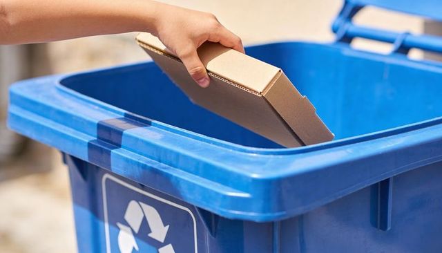Placing flattened cardboard into blue recycling bin at curb for sustainable recycling