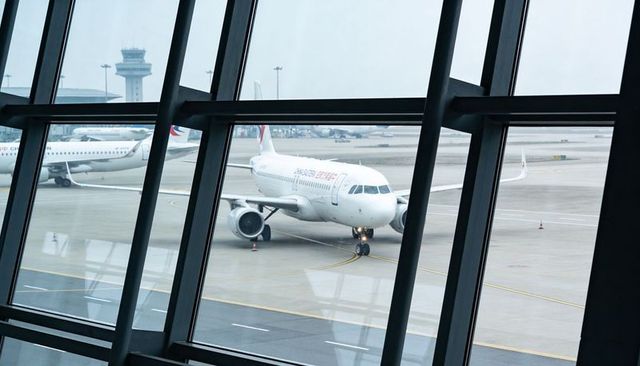 Framing narrow-body jet through terminal windows with control tower and airport apron