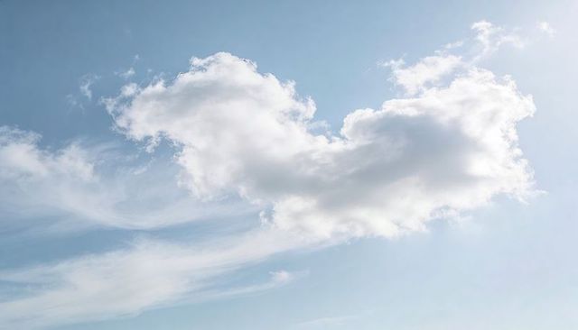 Drifting cumulus cloud forming soft heart shape over pale blue sky with wispy cirrus