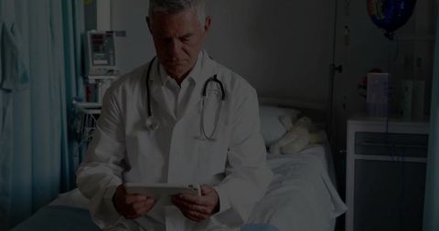 Senior doctor reviewing medical data on tablet in hospital room