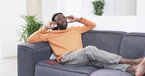 Relaxing african american man listening to music on sofa in bright modern living room