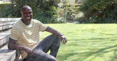 Smiling African American Man Relaxing on Bench in Sunlit Garden Wearing Striped Tee
