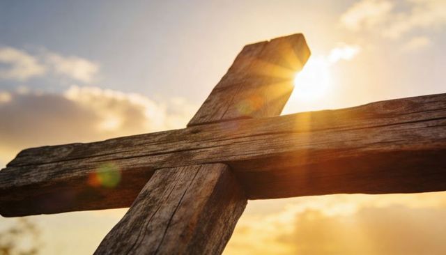 Sunlit weathered wooden cross silhouette at sunrise with golden lens flare and texture