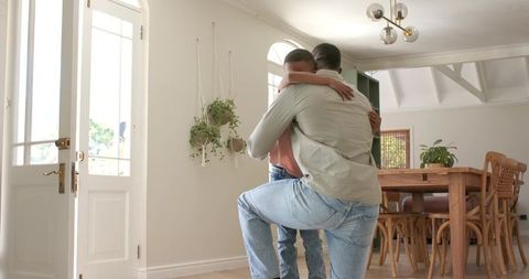 African american father hugging and lifting son at home entrance showing joyful reunion