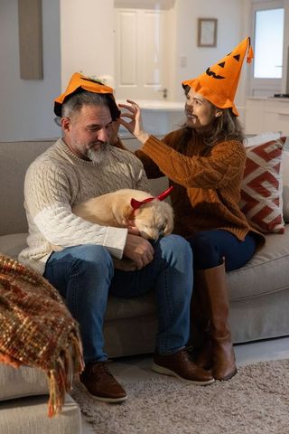 Couple wearing pumpkin hats adjusting costumes while cradling puppy with devil horns