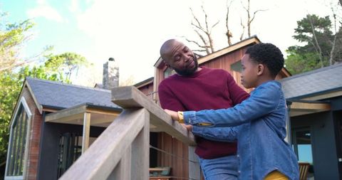 African american father and son leaning on deck railing at modern suburban home connecting