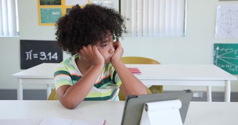 African American preteen looking distracted during tablet learning at classroom desk