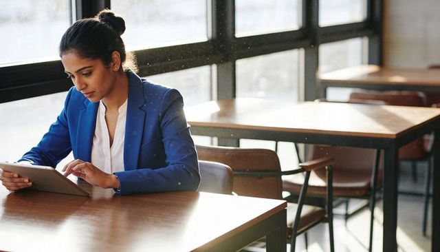 Indian businesswoman working on tablet in sunlit cafe with large windows