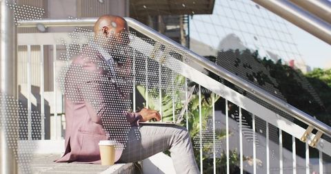 Mature businessman typing on laptop on urban steps with coffee cup and headphones