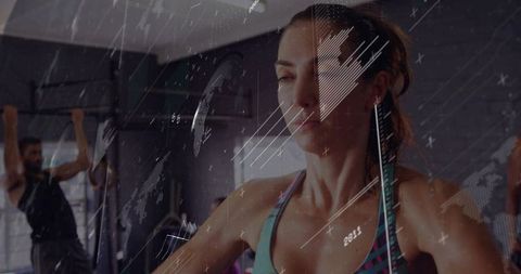 Determined woman training on cardio machine in gym with pull-up rig and textured overlay