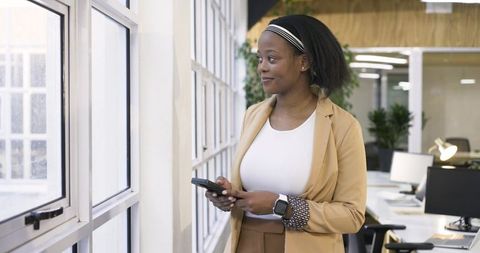 African american professional woman using smartphone and gazing out office window