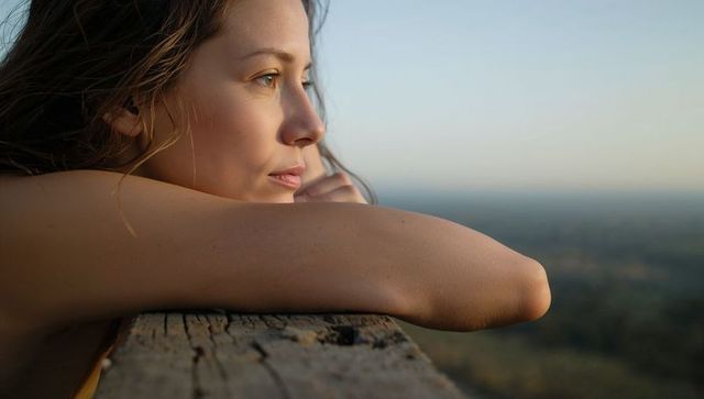 Young woman gazing from lookout resting on weathered wood railing contemplative portrait
