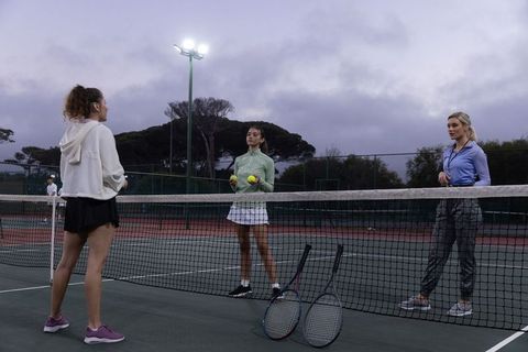 Female players standing at net holding tennis balls and rackets practicing twilight drills