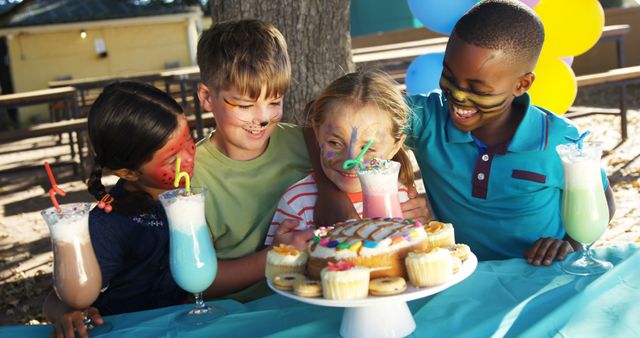 Children gathered outdoors, celebrating a birthday party with colorful cake and milkshakes. They are smiling and enjoying a happy moment together. Ideal for promoting birthday party events, kid's party supplies, or joyful childhood memories.