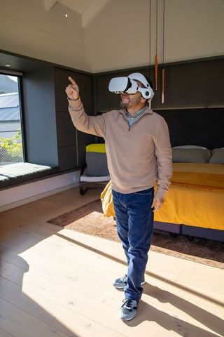 Middle-aged man exploring virtual reality in modern sunlit bedroom with yellow bedding