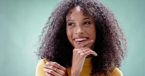 Smiling African American Woman Touching Chin Wearing Yellow Ribbed Top and Rings