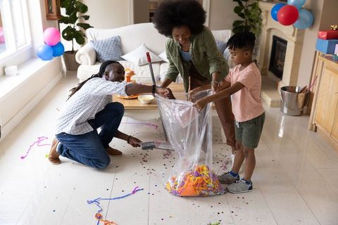 African american family cleaning up after birthday party with confetti and balloons at home