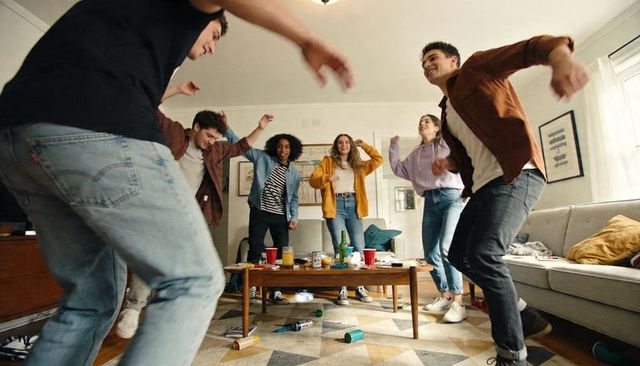 Friends dancing and laughing in living room during casual indoor house party