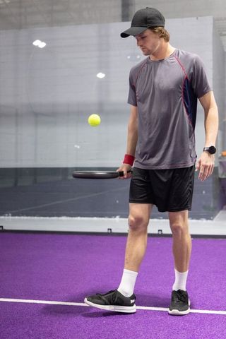 Young man practicing paddle tennis on purple indoor court watching ball