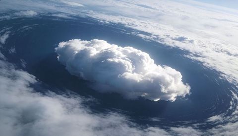 Sunlit towering cumulonimbus rising over swirling ocean thunderhead, dramatic cyclone sky