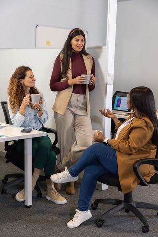 Female coworkers chatting over coffee in casual office corner, team collaboration moment