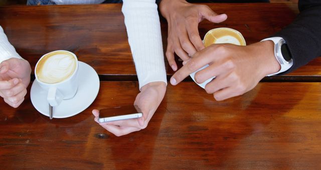 Two People Discussing over Coffee with Smartphone on Wooden Table - Download Free Stock Images Pikwizard.com