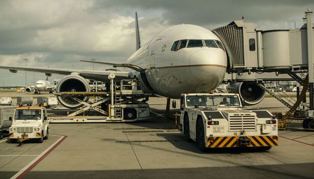 Wide-body jet undergoing servicing at busy airport gate with pushback tug and ground crew