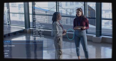Two colleagues discussing holographic data dashboards while collaborating in modern atrium