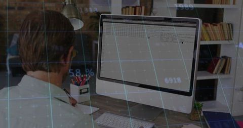 Man working at desk analyzing data on desktop computer with digital grid overlay