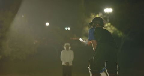 Floodlit night cricket moment with batsman facing bowler appeal while teammates cheer