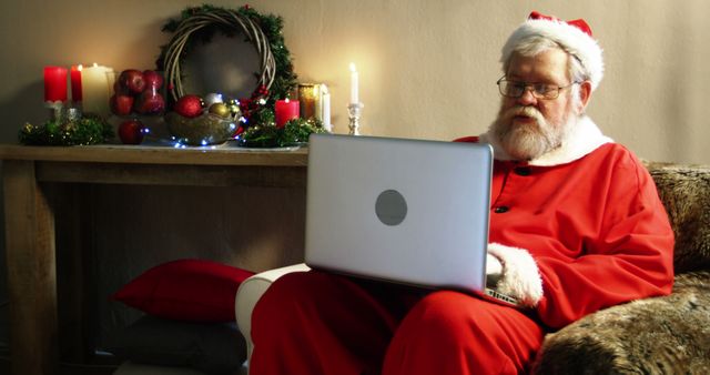 A Caucasian senior man dressed as Santa Claus is using a laptop, with copy space. His expression suggests he might be reading a list or managing holiday plans.