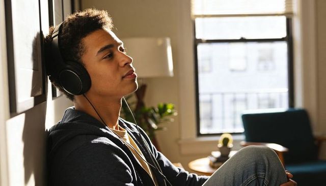 Teen listening to music with headphones relaxing in sunlit urban apartment lounge