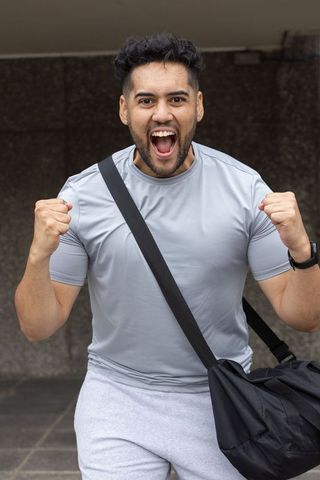 Triumphant african american athlete cheering, clenching fists, carrying duffel under overhang
