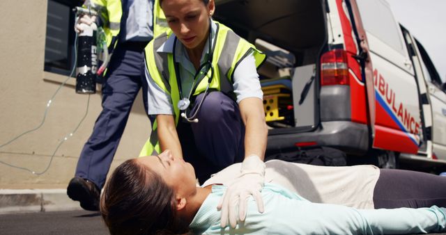 Paramedics are attending to an unconscious woman lying on the ground outside an ambulance. The medical team is providing immediate care with necessary equipment. This image can be used in contexts related to emergency medical services, healthcare, first aid training, and public safety awareness.