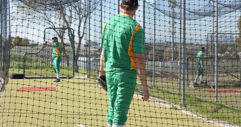 Baseball teammates practicing in netted cages wearing green and yellow uniforms