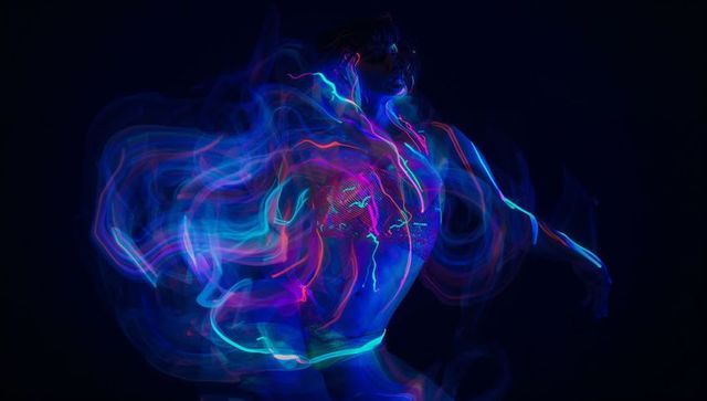 Dancing performer in dark studio with vibrant neon led light trails