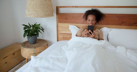 Relaxed Woman in Cozy Bedroom Using Smartphone
