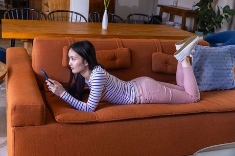 Asian woman reading messages on phone in relaxing living room