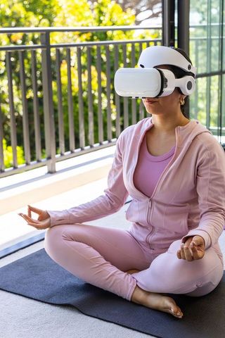 African american woman meditating with vr headset on balcony in pink activewear practicing calm