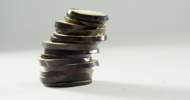 Sliced eggplant stacked in an angled arrangement on a light grey background. Highlighting fresh and organic produce, perfect for use in food blogs, vegetarian recipes, culinary magazines, and healthy eating promotions.