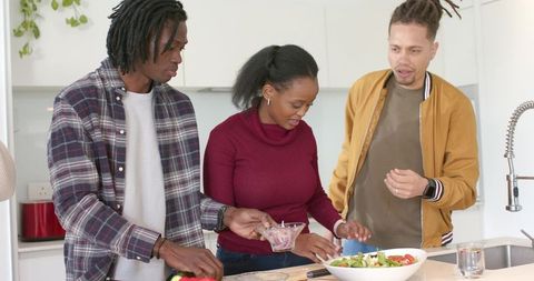 Diverse friends preparing healthy salad together at modern kitchen island, cooking lifestyle