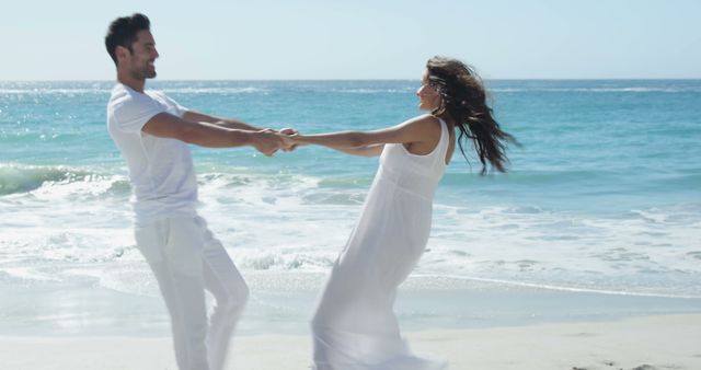 Couple spinning together near ocean showing fun and romance. Use for relationships, romance, summer vacations, beach holidays promotions, joyful moments posts.